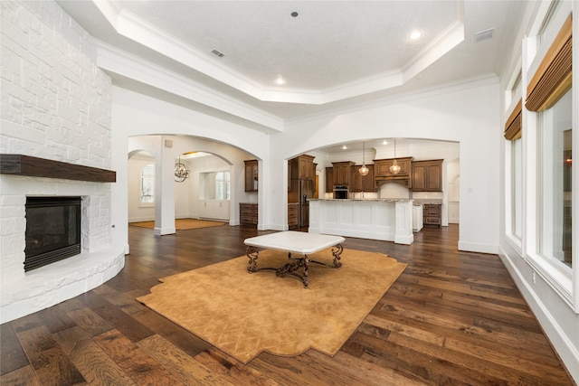 living room featuring crown molding, a tray ceiling, dark hardwood / wood-style flooring, and a stone fireplace