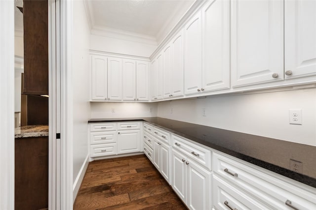 interior space with ornamental molding, dark countertops, dark wood-type flooring, and white cabinetry