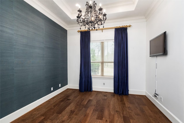 empty room featuring an accent wall, wood finished floors, baseboards, a tray ceiling, and crown molding