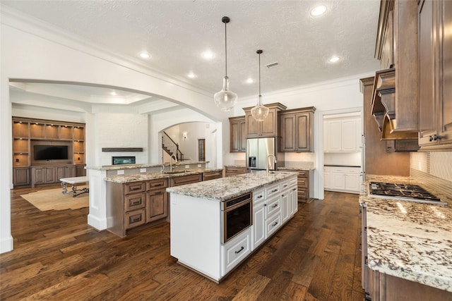 kitchen featuring pendant lighting, appliances with stainless steel finishes, dark hardwood / wood-style floors, light stone counters, and a large island with sink