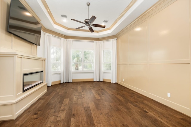 unfurnished room with a tray ceiling, a decorative wall, crown molding, and a glass covered fireplace