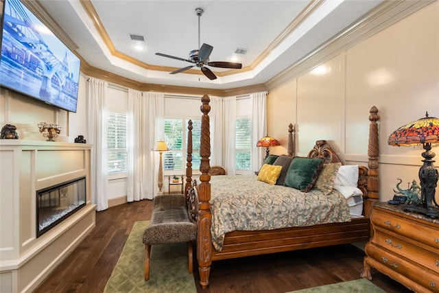 bedroom with a raised ceiling, ornamental molding, a glass covered fireplace, and visible vents