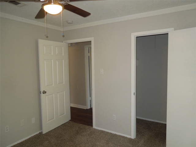 unfurnished bedroom with ceiling fan, ornamental molding, a walk in closet, a closet, and dark colored carpet