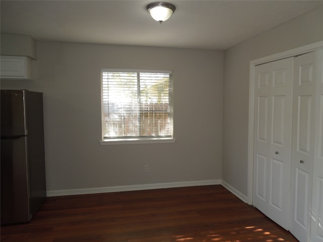 unfurnished bedroom with a closet, dark hardwood / wood-style floors, and stainless steel refrigerator