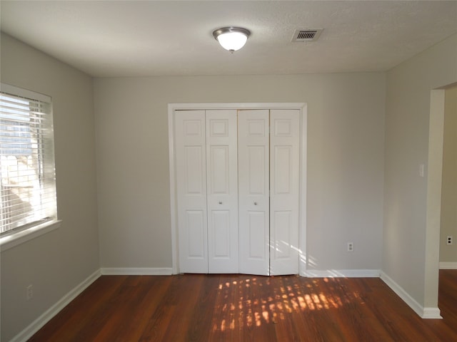 unfurnished bedroom with a closet, dark hardwood / wood-style floors, and a textured ceiling