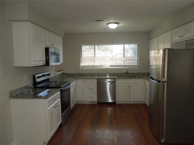 kitchen featuring white cabinets, stainless steel appliances, dark stone counters, dark hardwood / wood-style floors, and sink