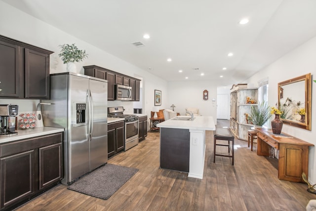 kitchen with dark wood-type flooring, sink, an island with sink, a kitchen breakfast bar, and stainless steel appliances