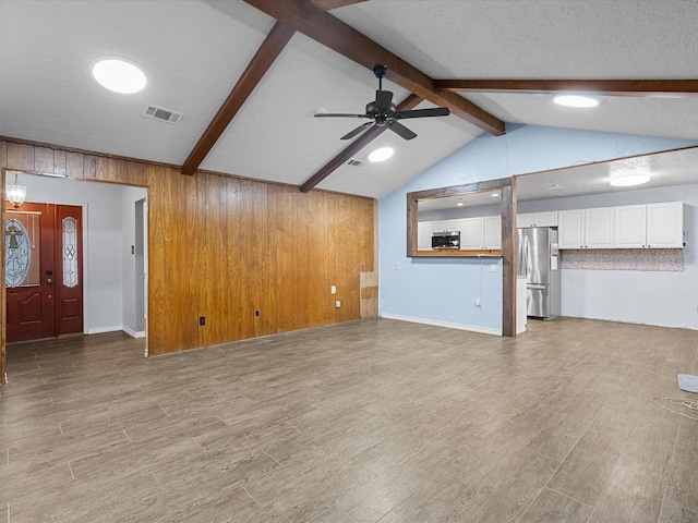 unfurnished living room featuring ceiling fan, lofted ceiling with beams, wood-type flooring, and wooden walls