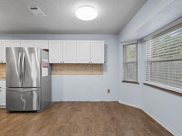 kitchen with stainless steel refrigerator, white cabinets, a textured ceiling, and hardwood / wood-style flooring