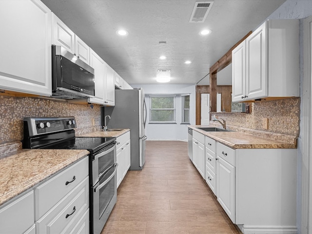 kitchen with decorative backsplash, appliances with stainless steel finishes, sink, light hardwood / wood-style floors, and white cabinetry