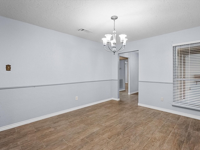 unfurnished room featuring a chandelier, wood-type flooring, and a textured ceiling