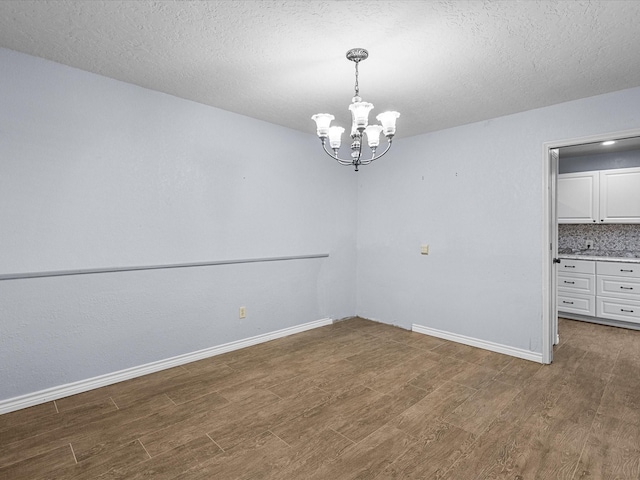 unfurnished dining area with a textured ceiling, a notable chandelier, and dark wood-type flooring