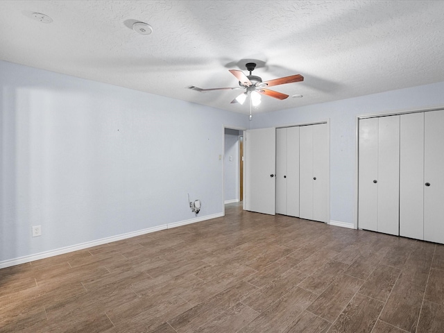 unfurnished bedroom featuring multiple closets, ceiling fan, wood-type flooring, and a textured ceiling