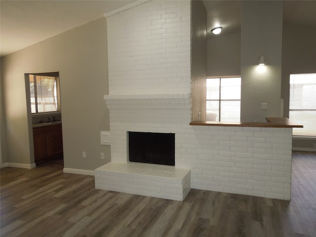 unfurnished living room featuring a brick fireplace, lofted ceiling, and dark hardwood / wood-style flooring