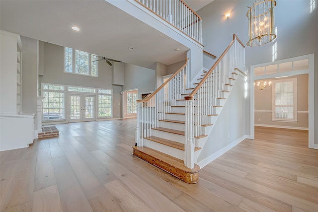 stairway with french doors, ceiling fan with notable chandelier, a high ceiling, and hardwood / wood-style flooring