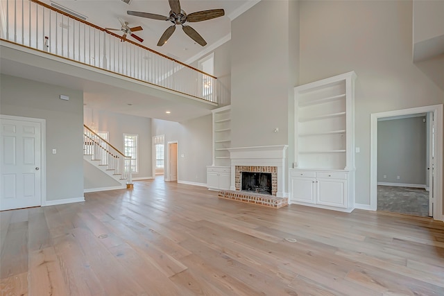 unfurnished living room featuring built in shelves, a towering ceiling, a fireplace, ornamental molding, and light hardwood / wood-style floors