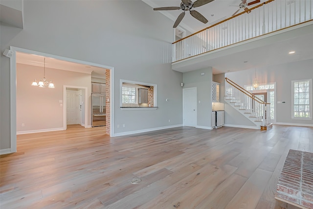 unfurnished living room featuring a high ceiling, ceiling fan with notable chandelier, and light hardwood / wood-style floors