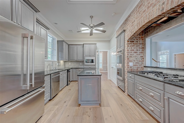 kitchen with appliances with stainless steel finishes, light wood-type flooring, a healthy amount of sunlight, gray cabinets, and a kitchen island