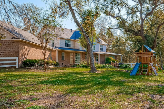 rear view of property featuring a playground and a yard