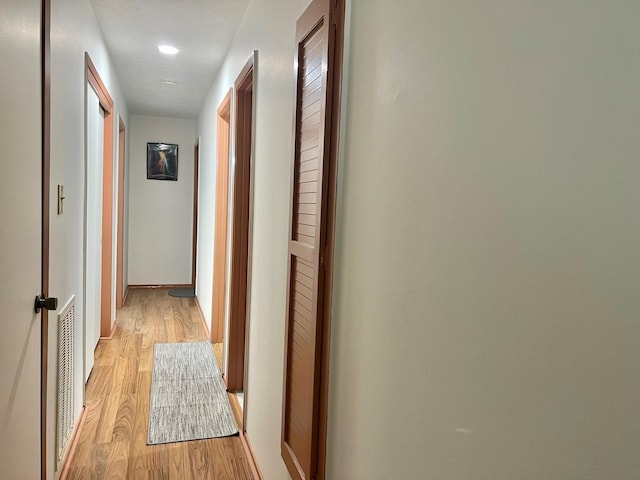 corridor with a textured ceiling and light hardwood / wood-style flooring