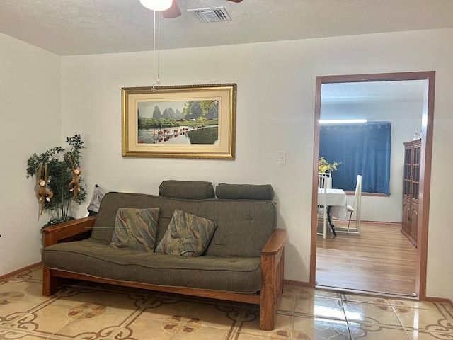 living room featuring light hardwood / wood-style floors, ceiling fan, and a textured ceiling