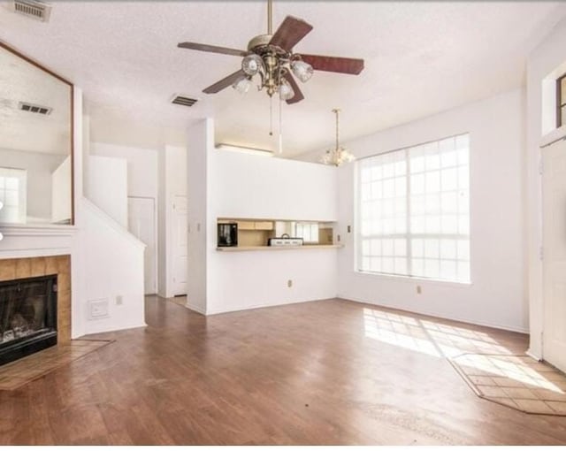 unfurnished living room featuring a tile fireplace, hardwood / wood-style floors, ceiling fan with notable chandelier, and a textured ceiling