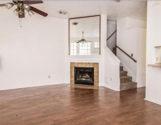 unfurnished living room featuring a tile fireplace, ceiling fan, dark hardwood / wood-style flooring, and a textured ceiling