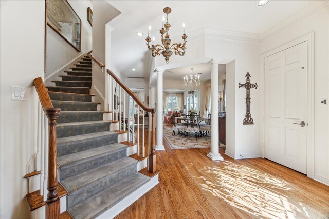 foyer with ornamental molding, a chandelier, light wood-type flooring, and ornate columns