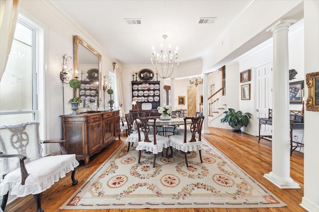 dining area with visible vents, decorative columns, a notable chandelier, and wood finished floors