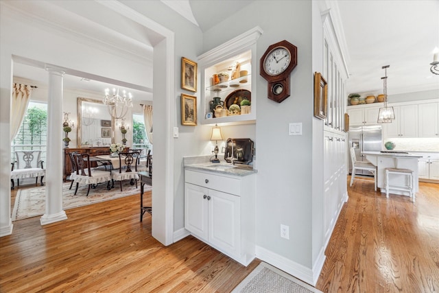 hall with light wood finished floors, baseboards, crown molding, ornate columns, and a chandelier