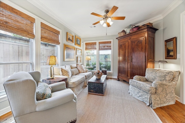 living area with visible vents, baseboards, ceiling fan, crown molding, and light wood-type flooring