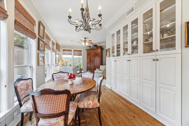 dining room featuring light wood-type flooring, visible vents, crown molding, and ceiling fan with notable chandelier