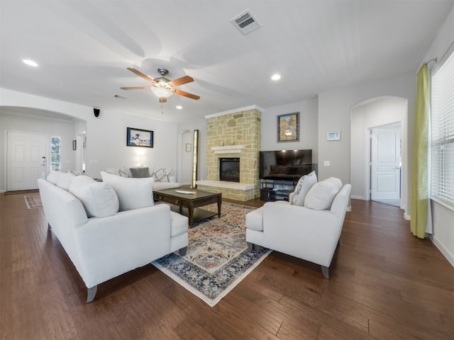 living room with ceiling fan, a stone fireplace, dark wood-type flooring, and a wealth of natural light