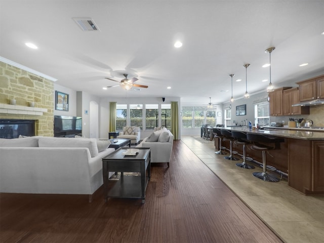 living room with ceiling fan, a stone fireplace, and dark wood-type flooring