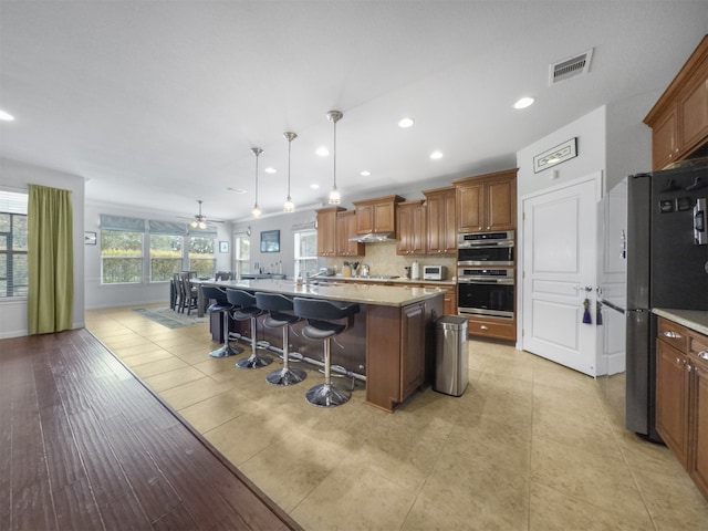 kitchen with appliances with stainless steel finishes, a kitchen breakfast bar, ceiling fan, decorative light fixtures, and a kitchen island with sink