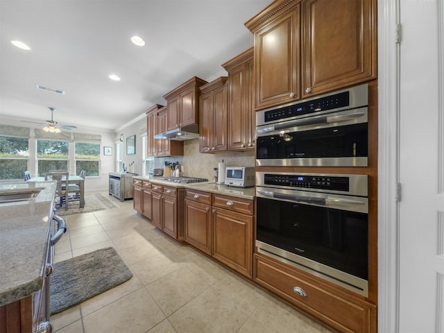 kitchen with ceiling fan, light tile patterned floors, ornamental molding, backsplash, and appliances with stainless steel finishes