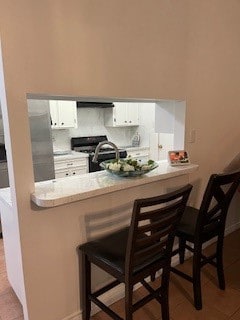 kitchen with white cabinets, black electric range, a kitchen breakfast bar, and kitchen peninsula