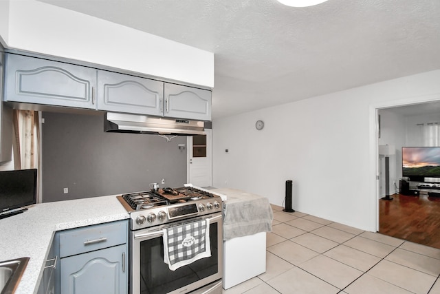 kitchen with a textured ceiling, gray cabinetry, light tile patterned flooring, and stainless steel stove