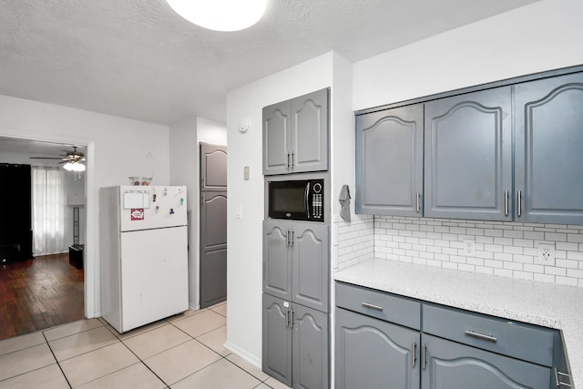 kitchen featuring gray cabinetry, light hardwood / wood-style floors, black microwave, white fridge, and ceiling fan