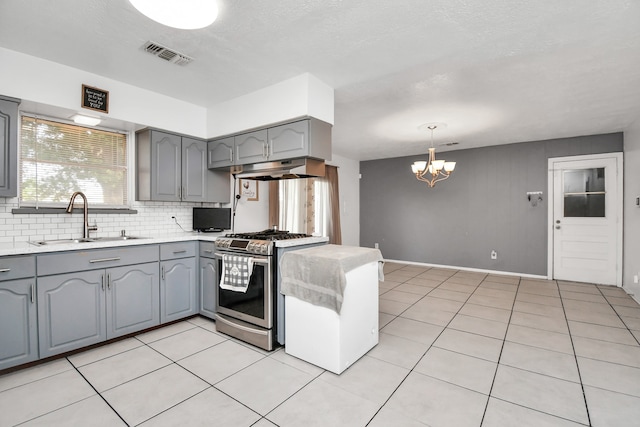 kitchen with a chandelier, stainless steel range with gas cooktop, sink, backsplash, and decorative light fixtures