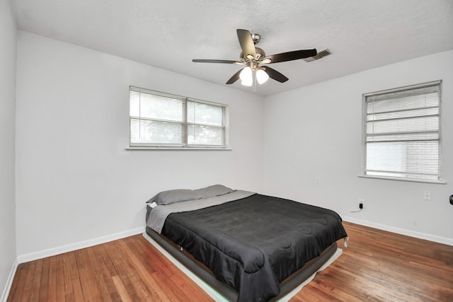 bedroom with multiple windows, a textured ceiling, ceiling fan, and hardwood / wood-style flooring