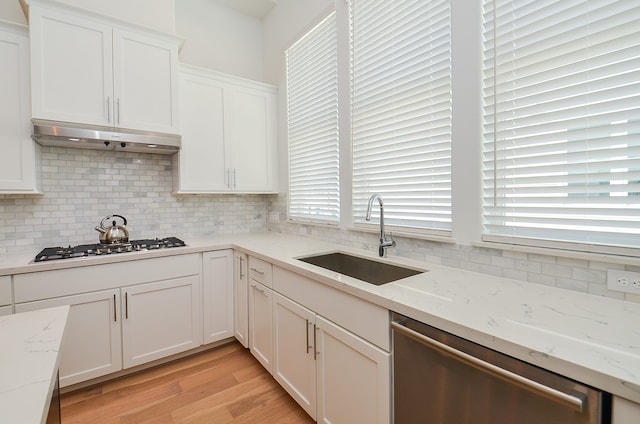 kitchen with light stone countertops, exhaust hood, stainless steel appliances, sink, and plenty of natural light