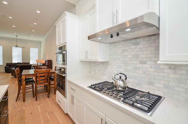 kitchen with light wood-type flooring, decorative backsplash, crown molding, stainless steel gas cooktop, and white cabinetry