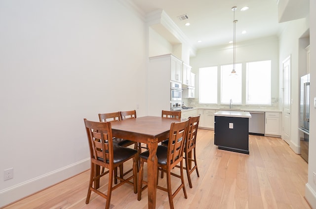 dining space with ornamental molding, sink, and light hardwood / wood-style floors