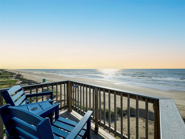 balcony at dusk featuring a beach view and a deck with water view