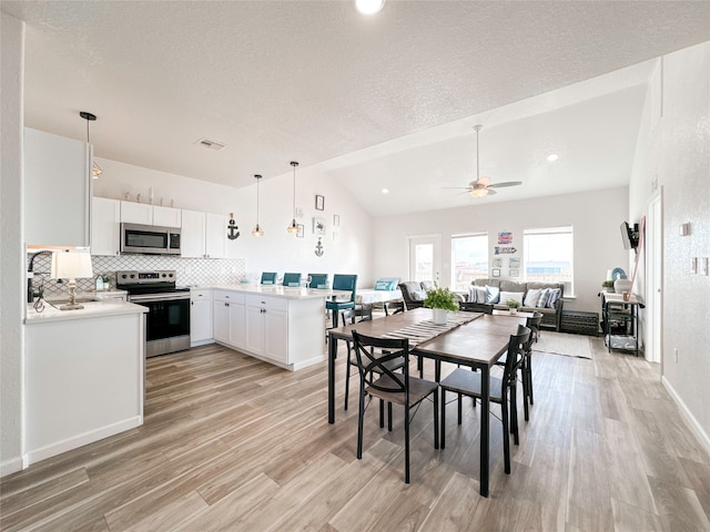 dining space with ceiling fan, a textured ceiling, light hardwood / wood-style floors, and vaulted ceiling