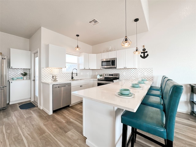 kitchen with appliances with stainless steel finishes, hanging light fixtures, a breakfast bar area, and white cabinets