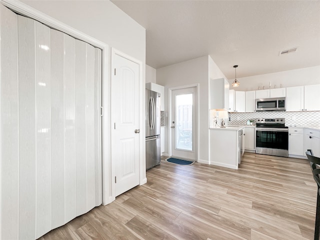 kitchen with light hardwood / wood-style floors, white cabinets, backsplash, stainless steel appliances, and decorative light fixtures