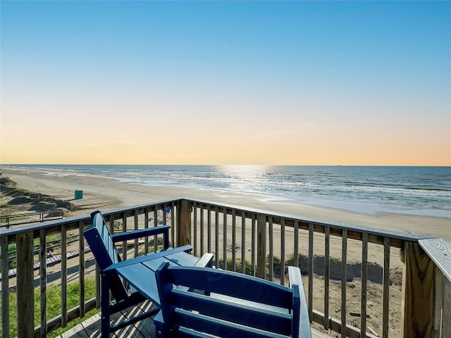 balcony at dusk featuring a water view and a view of the beach