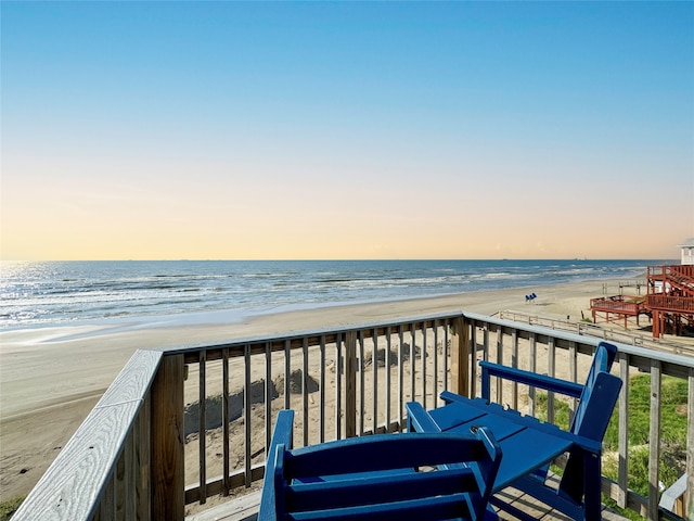 balcony at dusk featuring a beach view and a water view